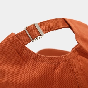 Detailed close-up of burnt orange baseball cap with adjustable metal slider buckle