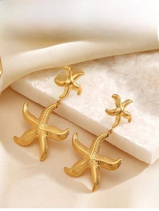 Close-up of golden starfish earrings with textured surface on white stone and silk