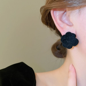 Close-up of black flocked flower earrings with matte texture on a model's ear