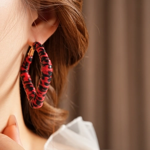 Close-up of a model wearing red and black leopard print woven hoop earrings in vintage style