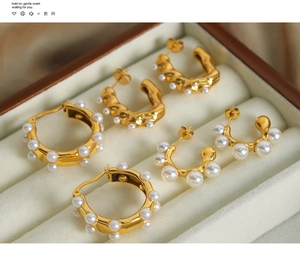 Macro detail of three-piece U-shape gold earrings with white pearls on a velvet tray