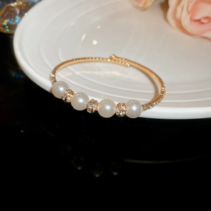 Detailed view of a gold open bangle featuring white pearls and shimmering pave diamonds