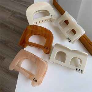Minimalist acetate hair claws with geometric D and B patterns on a white surface