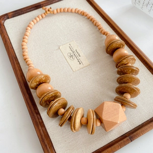 Detailed view of handcrafted wooden beaded necklace with geometric pendant on linen tray