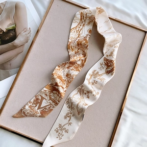 Detail of s-folded beige silk scarf with giraffe and nature prints on a velvet tray
