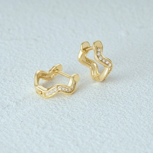 Macro shot of S925 sterling silver stamp on golden wavy earrings with tiny zircon crystals