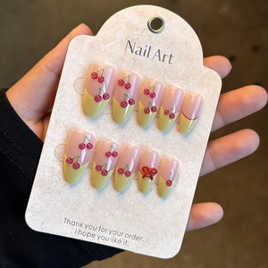 Detail of handmade press-on nails with 3D cherries and red metallic bows on a display card
