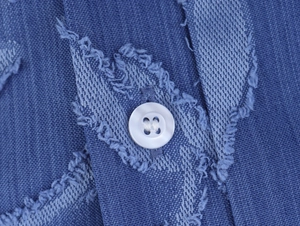 Gros plan détaillé du tissu denim jacquard bleu avec bouton blanc et texture frangée