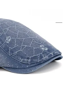 Detail of blue denim newsboy cap featuring white geometric embroidery and adjustable brim