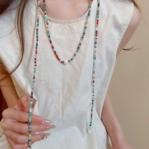 Close-up of bohemian colorful beaded necklace with white pearls on a model wearing beige