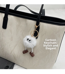 Dettaglio di un ciondolo in peluche bianco con grandi occhi su una borsa tote beige testurizzata