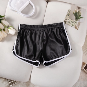 Detail of black satin yoga shorts with white trim and elastic waistband on a white sofa