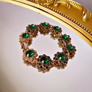 Dettaglio macro del bracciale vintage dorato a fiori con grandi strass verdi incastonati
