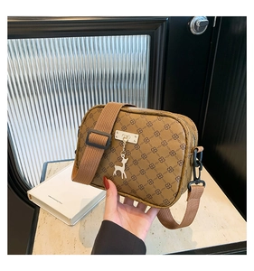 Close-up of brown monogram crossbody bag with metallic deer charm and wide shoulder strap