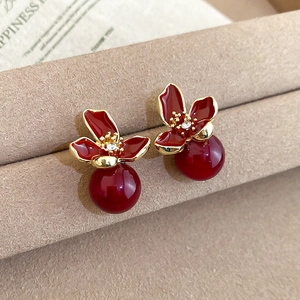 Detail shot of red floral earrings with golden edges and pearl drops on a display stand