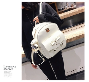 White PU leather backpack featuring bow decor and teddy bear charm on model back