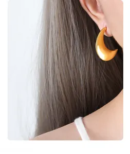Détail d'une boucle d'oreille demi-lune dorée polie portée par un mannequin femme