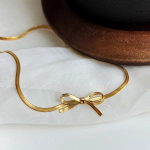 Golden bow pendant necklace with sleek snake chain texture on white fabric