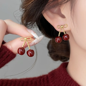 Close-up of elegant cherry bow earrings in wine red and gold on a model profile