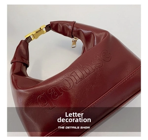 Detail of burgundy leather dumpling bag featuring embossed letters and golden metal buckle