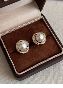 Detail of round pearl earrings with double gold zircon circles in a brown jewelry box
