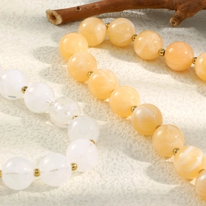 Dettaglio di braccialetti con perle bianche e giallo chiaro e distanziatori dorati in acciaio