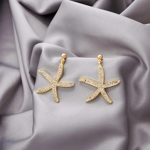 Macro shot of gold starfish earrings with sparkling crystals on grey silk fabric background