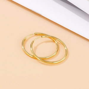 Polished gold round hoop earrings shown in a close-up detail on a minimalist background