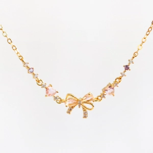 Detail view of gold O-chain necklace featuring a bow pendant with pink zircon inlays