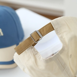 Adjustable silver metal buckle and brown strap detail on a beige cotton baseball cap