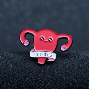Cute pink enamel uterus pin with Cuterus ribbon on a black textured background