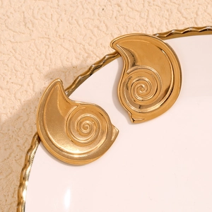 Golden spiral ear studs in 18K gold plated stainless steel on elegant ceramic plate