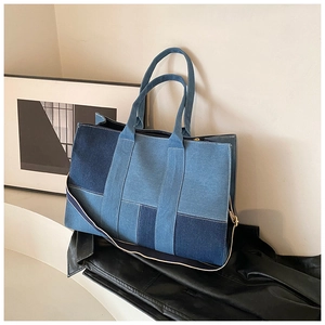 Detail of a large denim patchwork tote bag with adjustable strap on a white platform