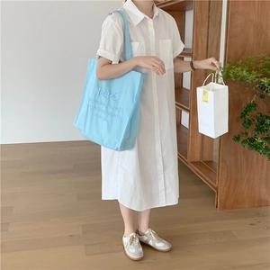 Lifestyle-Foto der hellblauen Canvas-Tasche mit Bebe-Stickerei und weißem Hemdkleid