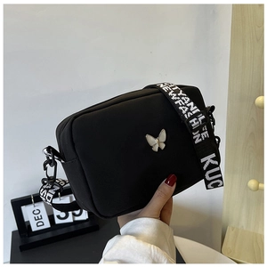 Close-up of black nylon crossbody bag featuring a butterfly charm and patterned wide strap