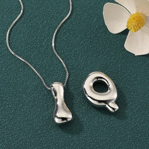 Macro detail of silver letter Q and I pendants on a minimalist chain for hip-hop style