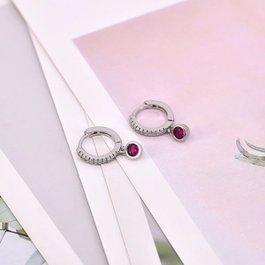 Close-up of silver earrings with round red zircons and sparkling pave-set white crystals