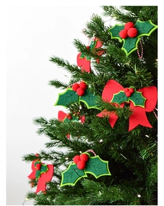 Close-up of Christmas felt holly leaves with red berries and bow on green tree branch