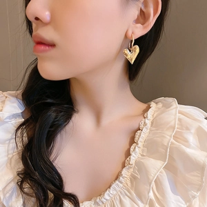 Détail d'une boucle d'oreille cœur dorée avec texture martelée portée par un modèle