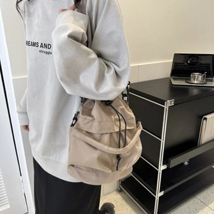 Sac seau en nylon beige avec cordon de serrage et bandoulière porté par un mannequin