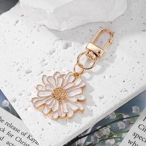 Daisy flower keychain with white enamel petals and gold metal clasp on stone background