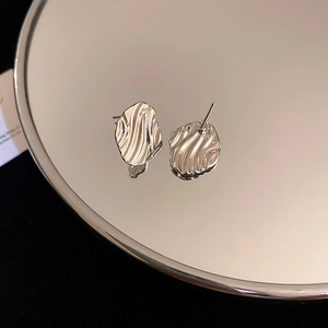 Macro shot of silver liquid ripple irregular geometric stud earrings on a mirror