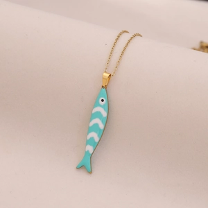 Macro detail of a golden chain necklace featuring a blue and white enamel fish pendant