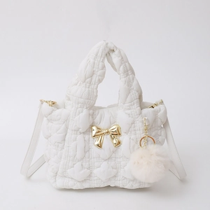 Détail d'un sac à main en nylon blanc matelassé avec nœud doré et pompon en peluche