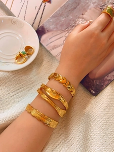 Detailed close-up of golden feather and twisted bracelets set on a female wrist