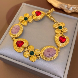 Close-up of vintage gold bracelet with red hearts and pink cameo charms on jewelry box