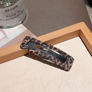 Close-up of leopard print fabric BB hair clip on a wooden tray with fashion props
