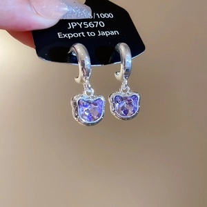 Macro detail of silver cat-shaped earrings with sparkling purple heart crystals