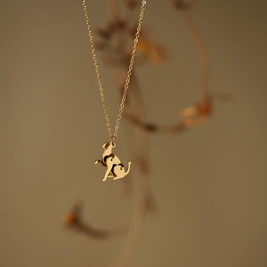 Close-up of golden cat pendant necklace with polished finish on warm floral backdrop