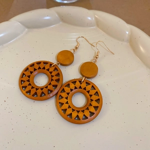 Close-up of bohemian hollow carved wooden sun earrings with golden metal clips
